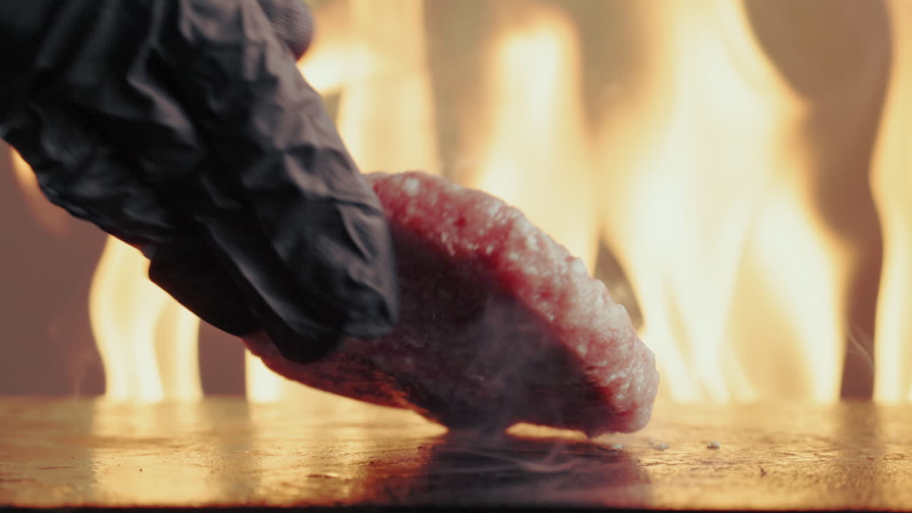Hamburger patty being cooked on a grill with flames