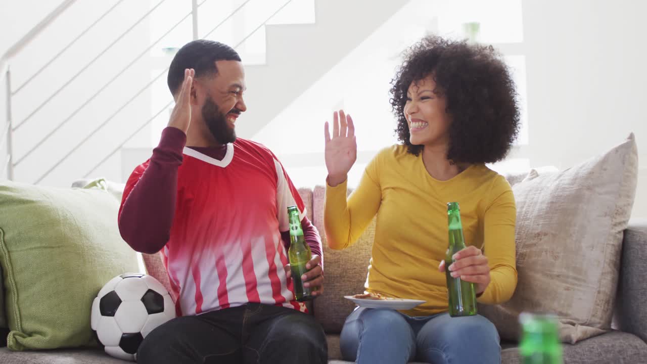 Couple cheering while watching sports on TV at home