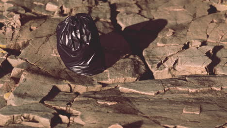 black trash bag lay on a rocky beach