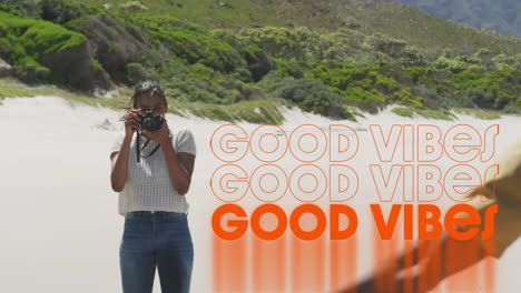 animación de las palabras buenas vibraciones escritas en naranja sobre una mujer en la playa tomando fotos de un amigo masculino