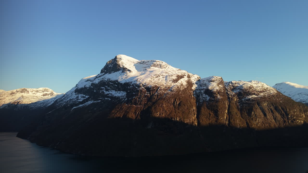 Et majestætisk sneklædt bjerg i Norge bades i varmt lys fra den gyldne time. Ideel til rejsepromovering og naturdokumentarer.