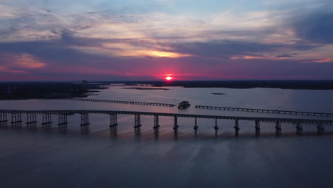 drone shot of beautiful pink sunset overlooking ocean and bridge in mississippi