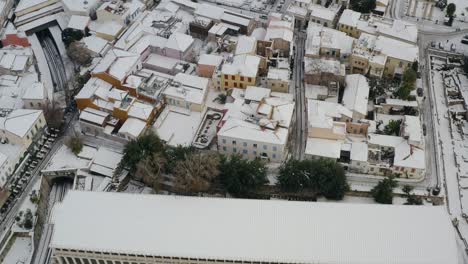 Vista-Aérea-Sobre-Casas-Cubiertas-De-Nieve-En-Atenas,-Raro-Día-De-Invierno-En-Grecia---Inclinación,-Disparo-De-Drones