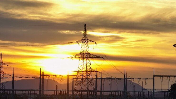 Linhas e torres de energia erguem-se em uma área rural ao pôr do sol, criando uma silhueta marcante