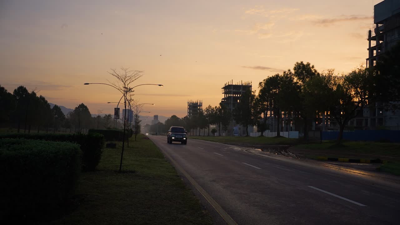 A beautiful cinematic morning view of Islamabad with a yellowish sky with sunrise and buildings under construction on Margalla Road while cars are passing by