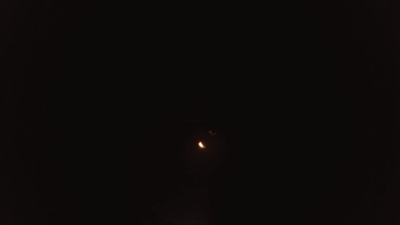 젊은 금발 남자가 검은 바탕의 안테나에서 밤에 불공을 만드는 큰 불의 흐름을 호흡합니다.