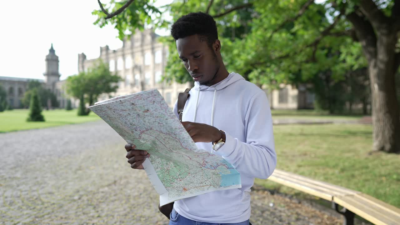 retrato de un joven afroamericano concentrado con un mapa de papel de pie en el campus universitario examinando rutas. estudiante guapo enfocado estudiando en un país extranjero. inteligencia y educación.