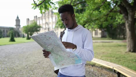 portrait of concentrated african american young man with paper map standing at university campus examining routes. focused handsome student studying in foreign country. intelligence and education.