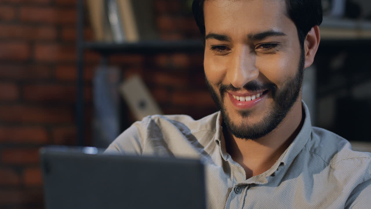 hombre de negocios árabe viendo algo en la tableta y sonriendo en la oficina