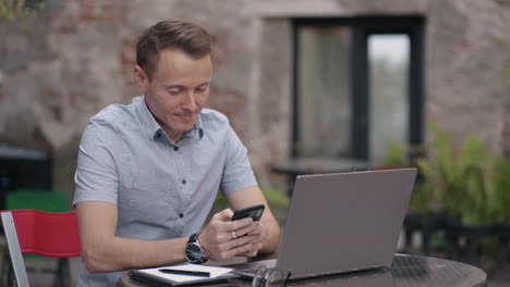 primer plano un hombre con un teléfono móvil está involucrado en la banca en línea compra en internet y escribe mensajes en las redes sociales mientras está sentado con una computadora portátil