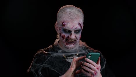 Frightening-man-Halloween-zombie-using-mobile-phone-typing-new-post-on-web,-browsing,-addiction