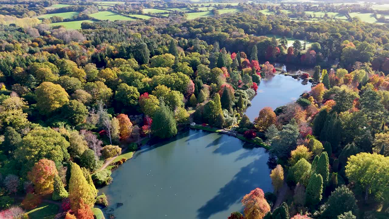 Stunning aerial panorama of the Sussex countryside during peak autumn. Woods, meadows, and shimmering water reflect the spectacular seasonal change in vivid colour