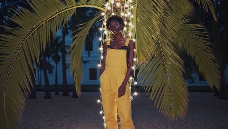 woman in yellow jumpsuit under palm trees at night