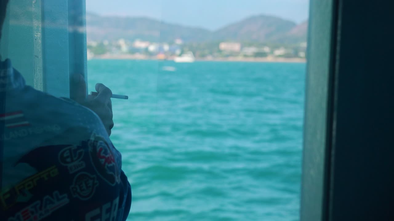 A person smokes on a fishing boat with scenic ocean views near Ko Racha Yai, Phuket. Bright daylight enhances the tranquil atmosphere