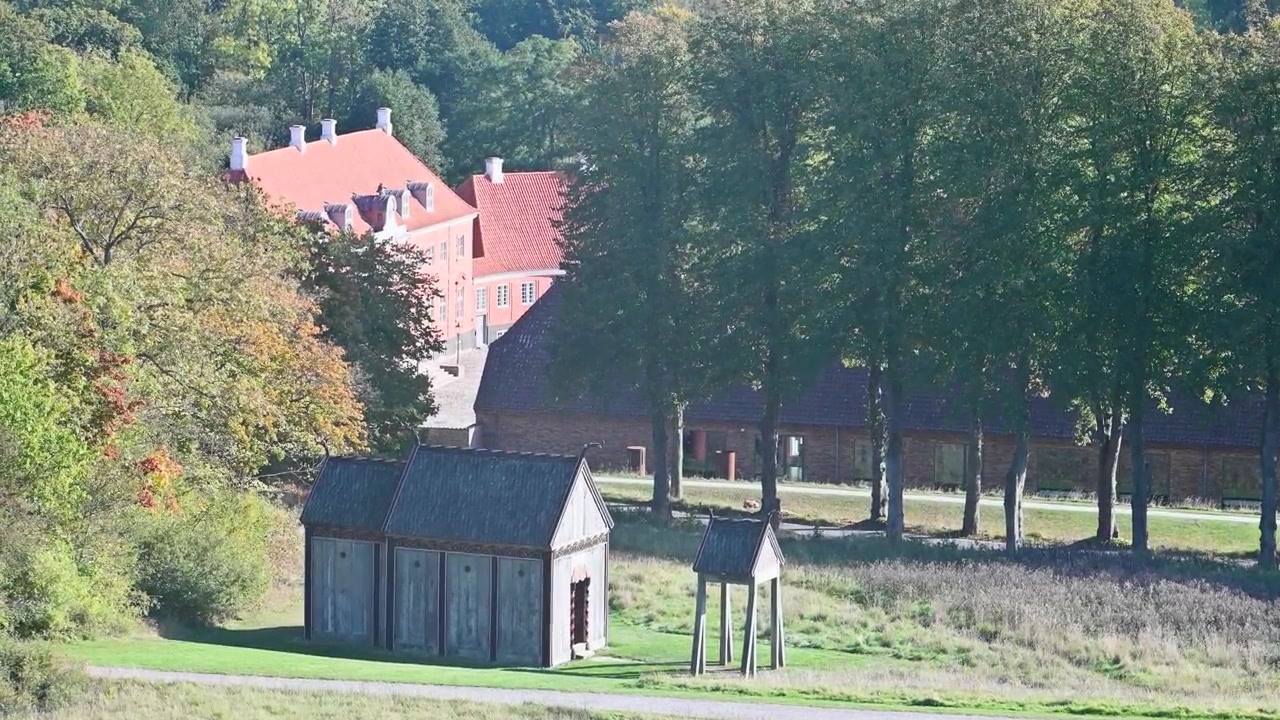 Luftfoto av en park med frodig grøntområde og en stor mursteinsbygning under en klar himmel