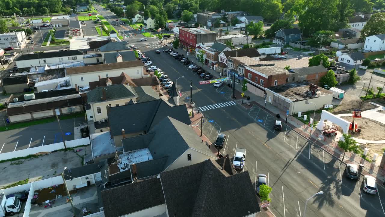 Strada principale di Egg Harbor, New Jersey, con edifici bassi in mattoni, vetrine di negozi, attraversamento pedonale, auto parcheggiate e case storiche sotto la luminosa luce solare estiva. Ripresa aerea in ascesa. Atmosfera tranquilla negli USA.