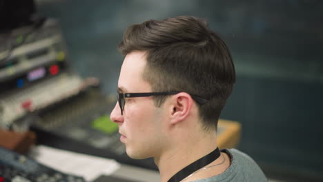 young man with glasses focused on computer screen in office environment, working on digital content or broadcast tasks, close-up shot in modern studio or control room