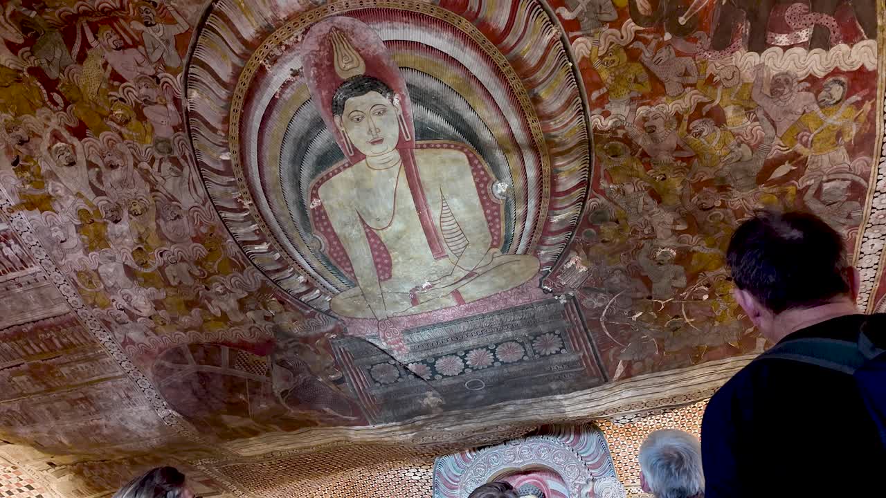 Tour guide elucidates the intricate depictions of Buddha on the ornate ceiling of Dambulla Cave Temple. Low Angle shot