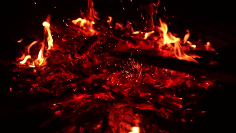 burning out pieces of wood in the campfire. unknown person moves the charcoal and sparkles fly up. close up. darkness at backdrop.