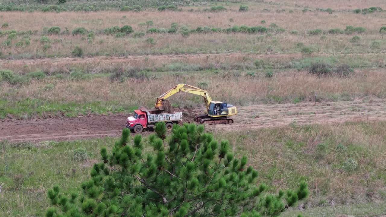 Aerial view of an excavator loading a red truck while working in a dry field.