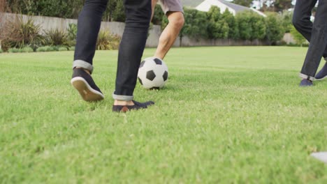 Diverse-male-friends-playing-football-in-garden-on-sunny-day