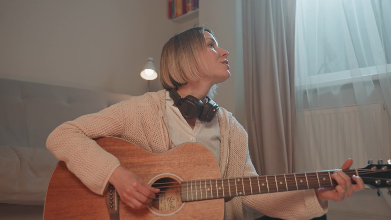 Guitarist plays peacefully. Comfortable woman with headphones creates soothing melodies seamlessly. Relaxed female guitar player produces calming tunes while immersed in cozy surroundings