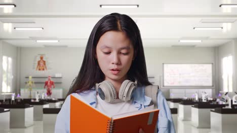 close up of asian teen girl student with a backpack reading book and having a headache while standing in science laboratory