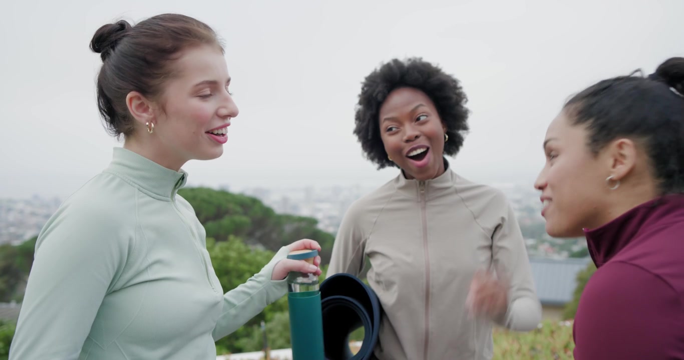 Diverse women friends meeting on hilltop, exchanging teal bottle, holding navy mats for workout
