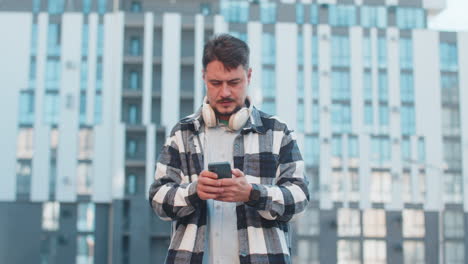 joven feliz poniendo auriculares escuchando música enérgica favorita en el teléfono inteligente en la calle