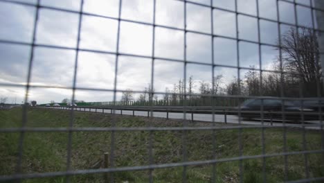 Vista-Desde-La-Cerca-De-Acero-De-Camiones-Y-Autos-Que-Pasan-Por-La-Carretera-En-Zlotoryja,-Polonia-En-Un-Clima-Nublado---Toma-Panorámica