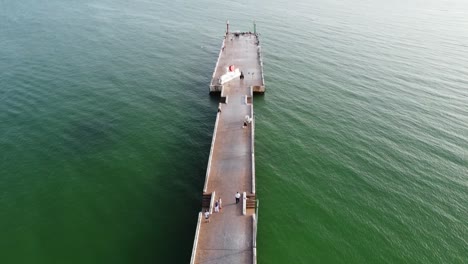 drone-shot-over-walking-pier-green-sea-ocean-horizon-forward