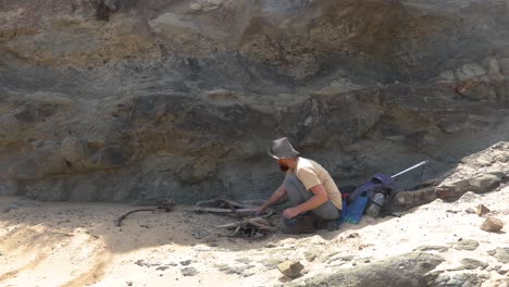 a wide shot of a bushman cooking a fish on hot coals on the coastline in australia