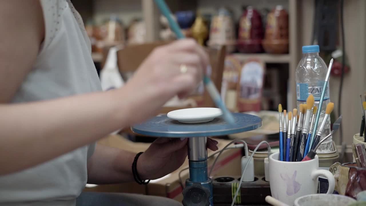 Female potter paint brushing ceramic plate at workshop for decorative artistic style, Gimbal shot