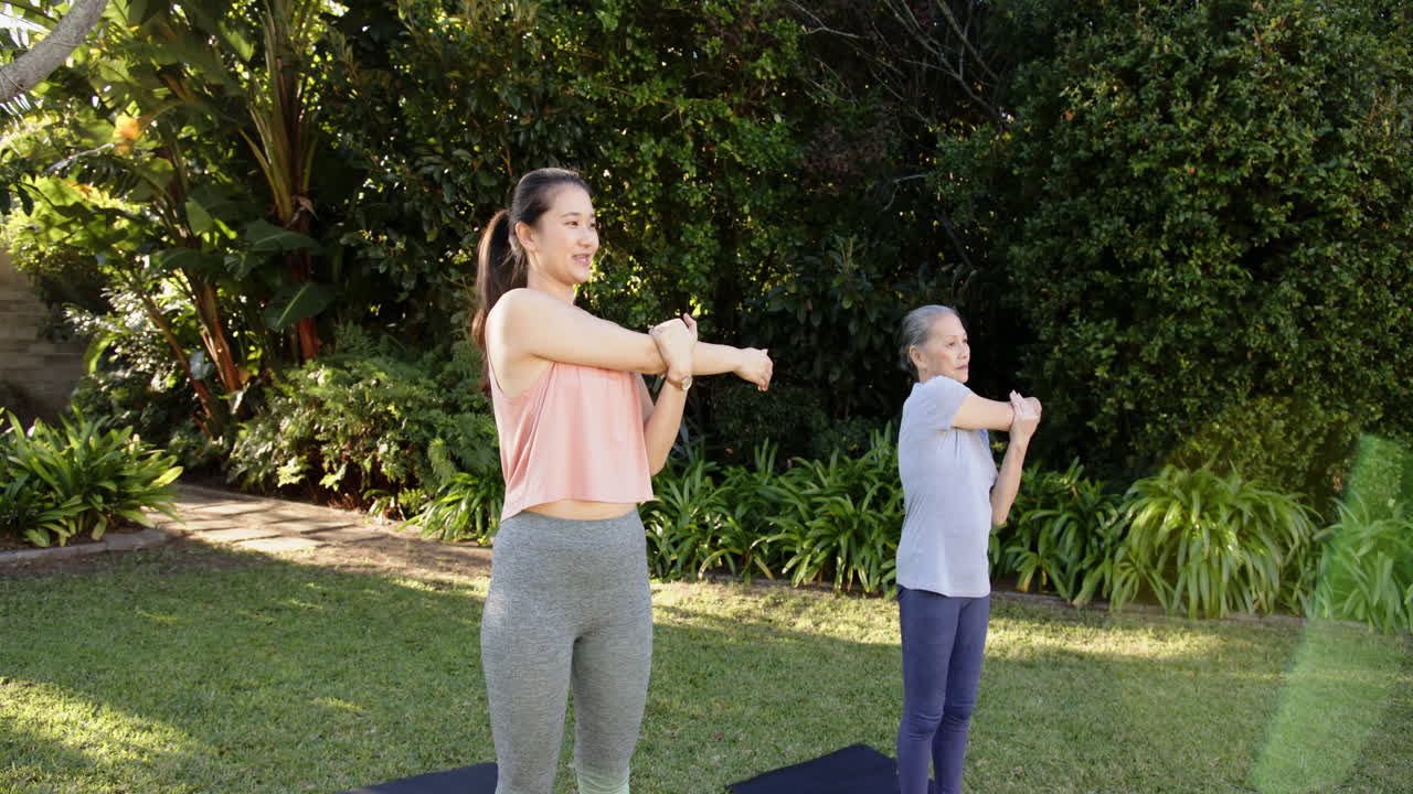 Exercising outdoors, Asian grandmother and granddaughter stretching on yoga mats in garden