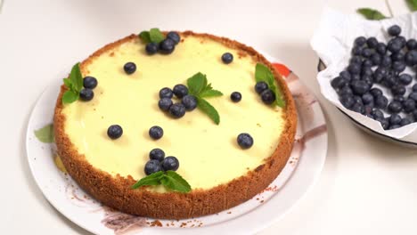 homemade cheesecake hand decorating with blueberry berries and mint leaves.