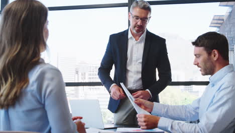 Business-Team-Meeting-Around-Office-Boardroom-Table-With-Laptops-Discussing-Documents