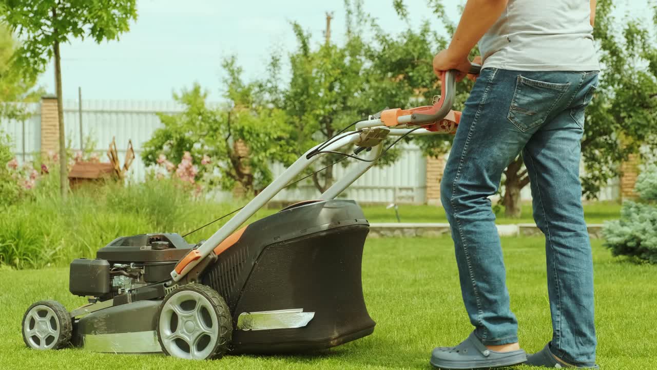 Lawn mower cutting the grass. Gardening activity. Cutting grass with petrol driven lawn mower in sunny garden. Gardener working with  mower machine in the garden. Lawn mower cutting green grass