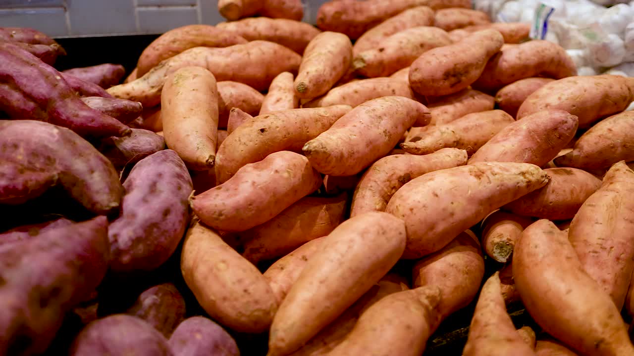 A vibrant assortment of sweet potatoes arranged in a supermarket setting, showcasing diverse colors and textures under bright lighting