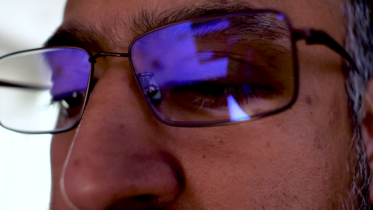 Adult man experiencing eye strain from computer screen light reflection in his glasses