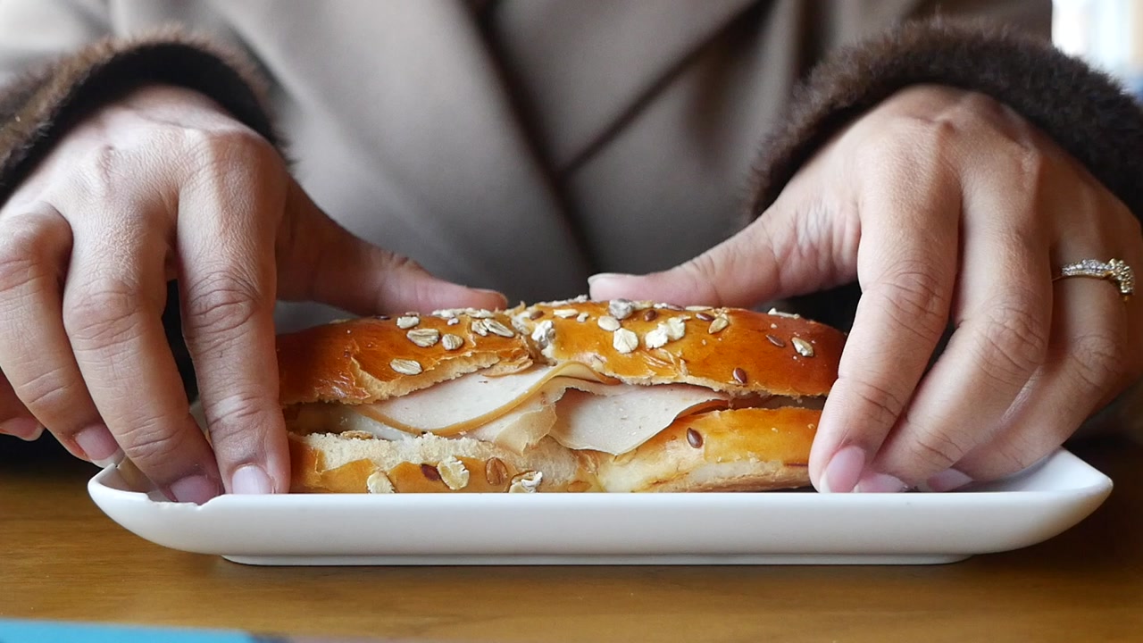 Hands Picking Up a Savory Deli Sandwich from a White Plate