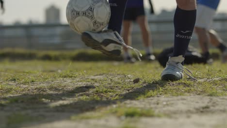 football soccer player balancing the ball on one foot on a dirt field during a sunny day