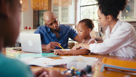 Familia-Alrededor-De-Una-Mesa-En-Casa-Usando-Una-Computadora-Portátil-Con-Padres-Ayudando-A-Los-Niños-Con-La-Tarea-De-Ciencias