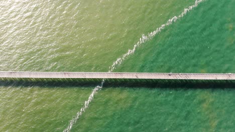 Top-down-right-to-left-sweep-of-a-long,-busy,-wooden-pier-stretching-into-the-gorgeous,-tropical,-lime-green-and-denim-blue-ocean-on-a-perfectly-warm-and-sunny-day