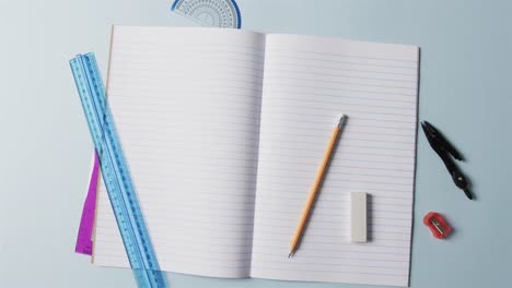 overhead view of open notebook with school stationery on blue background, in slow motion