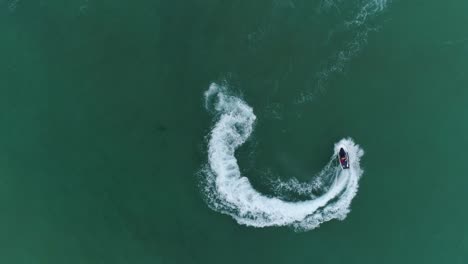 4k straight down zoom out spectacular aerial view of man having fun riding a personal watercraft in the ocean making a figure of eight pattern, mozambique