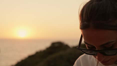 retrato de una joven pensativa con gafas de sol mirando hacia abajo con el sol poniéndose en el fondo