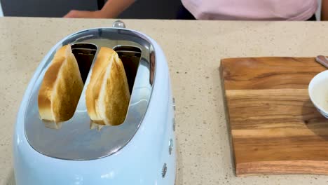 two slices of bread pop up from a retro blue toaster on a kitchen counter, with natural lighting and a steady, close-up camera angle