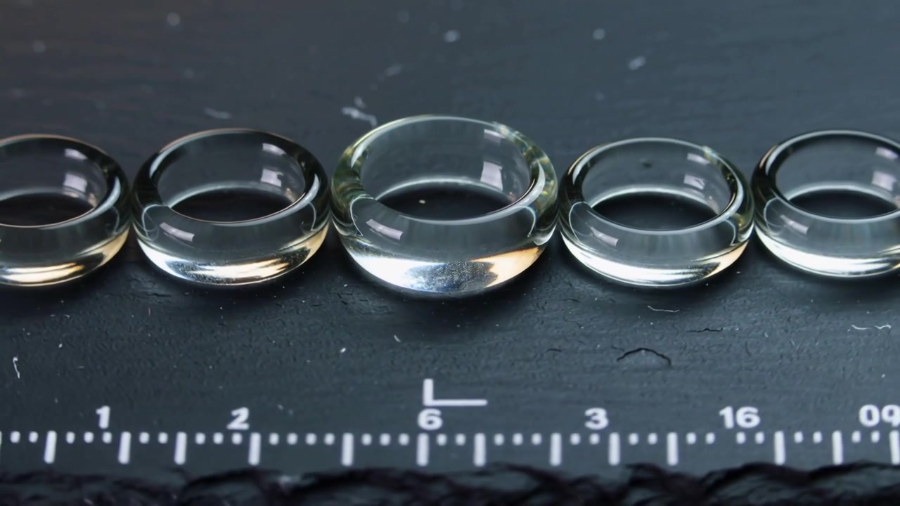 Moving camera shifting focus across clear glass donut rings on dark slate, highlighting ruler scale