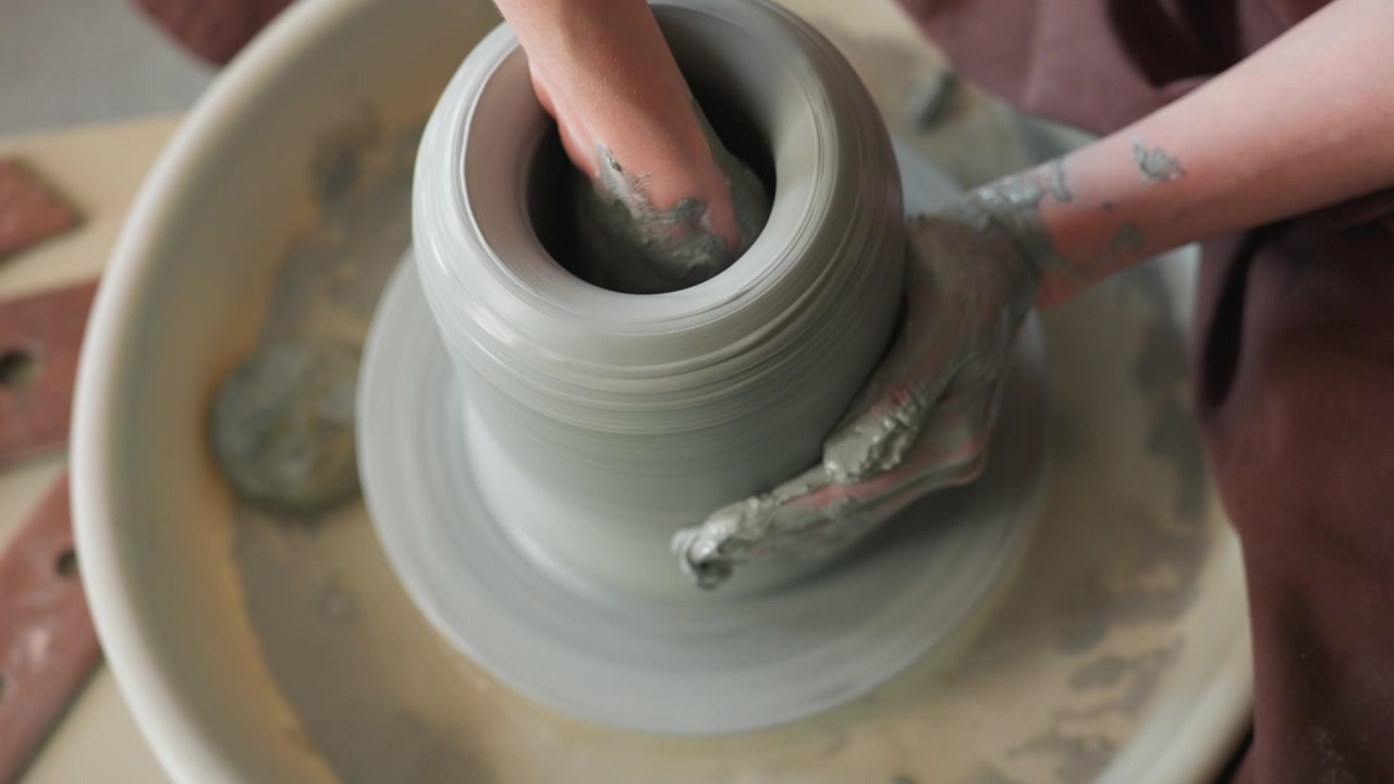 Closeup fingers hollowing clay into vase on spinning wheel, focused artisan finishing rim and refining texture, steady motion and fine tool work produce smooth profile, warm studio lighting emphasizes