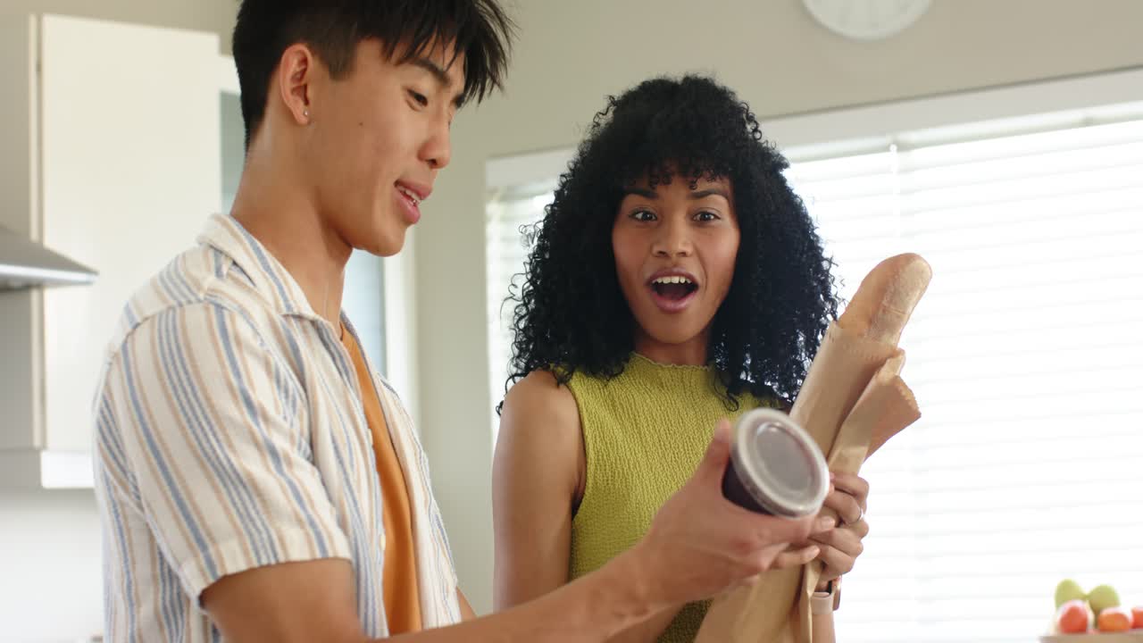 Baguette scent driving diverse couple sniffing and offering jam to surprise partner in kitchen